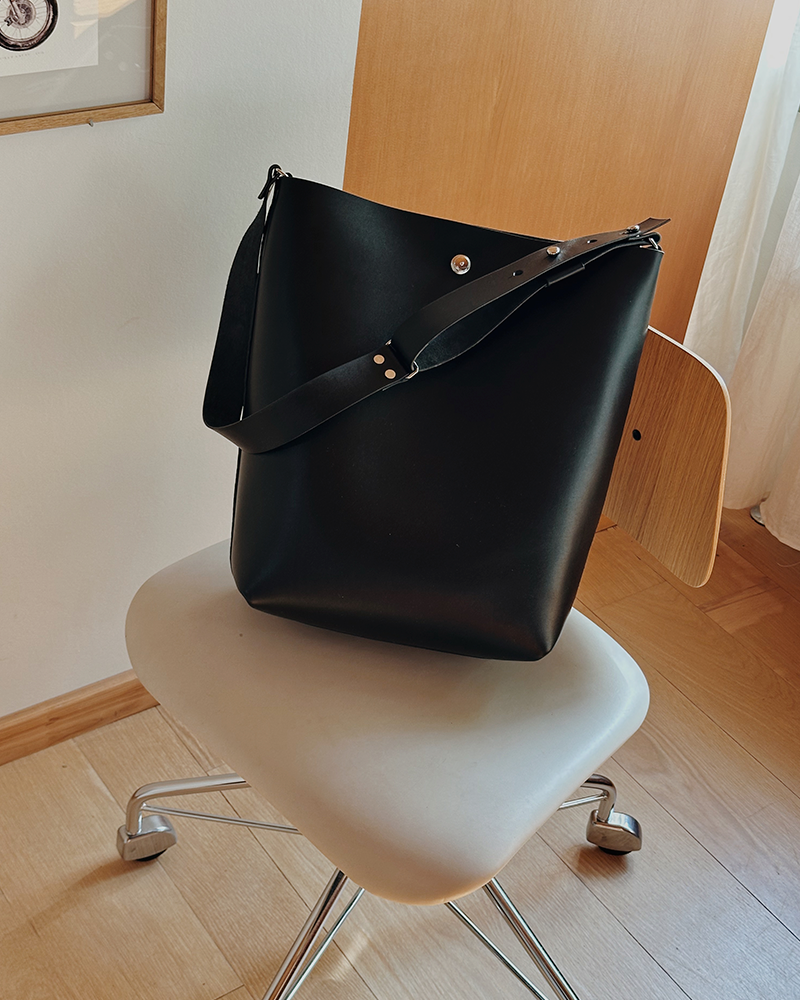 En minimalistisk og funktionel skuldertaske i sort kernelæder, designet til både hverdag og arbejde. Tasken rummer ét stort hovedrum med god plads til de ting, du har brug for – uanset om det er computer, dokumenter eller personlige ejendele. De brede stropper, monteret med solide nitter, gør den behagelig at bære over skulderen, og læderet vil med tiden udvikle en smuk patina, som gør hver taske unik. En enkel og tidløs taske, der kombinerer æstetik med holdbarhed – skabt til at følge dig i mange år fremover.