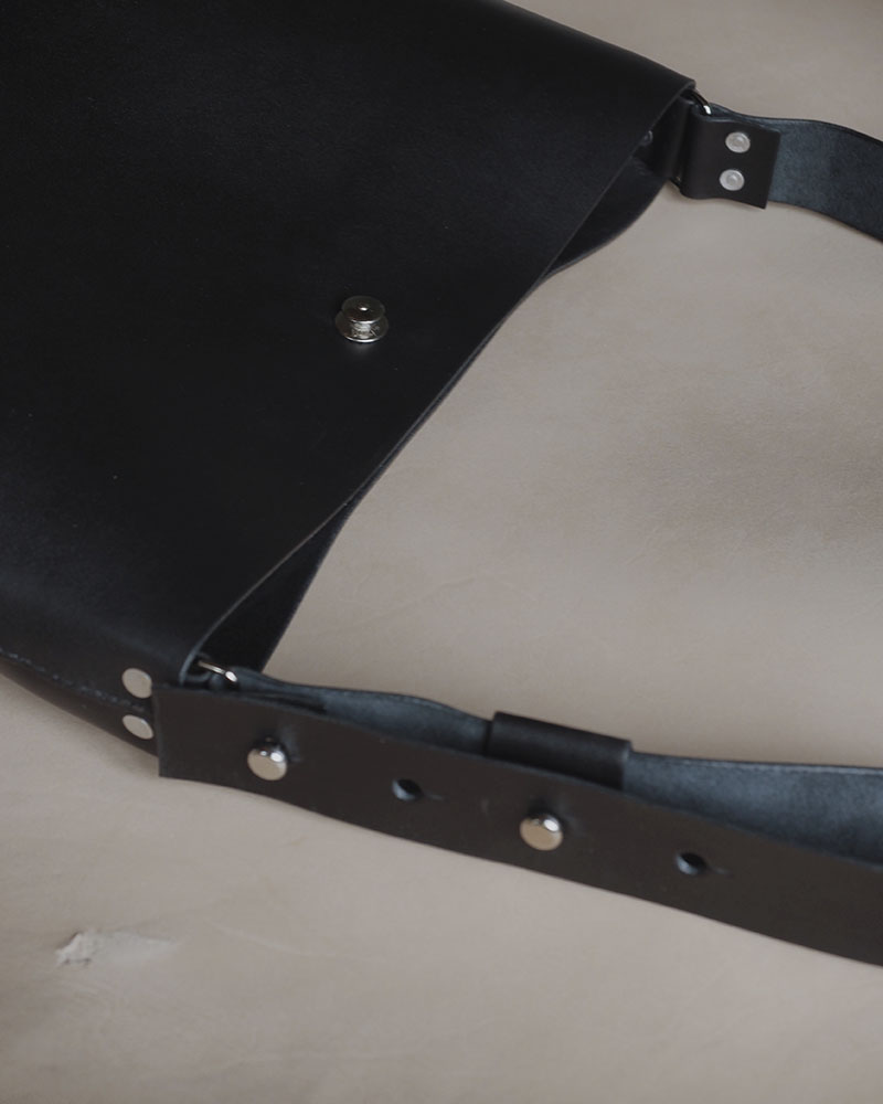 En minimalistisk og funktionel skuldertaske i sort kernelæder, designet til både hverdag og arbejde. Tasken rummer ét stort hovedrum med god plads til de ting, du har brug for – uanset om det er computer, dokumenter eller personlige ejendele. De brede stropper, monteret med solide nitter, gør den behagelig at bære over skulderen, og læderet vil med tiden udvikle en smuk patina, som gør hver taske unik. En enkel og tidløs taske, der kombinerer æstetik med holdbarhed – skabt til at følge dig i mange år fremover.