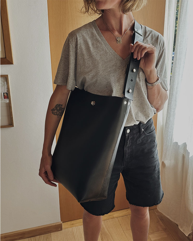 En minimalistisk og funktionel skuldertaske i sort kernelæder, designet til både hverdag og arbejde. Tasken rummer ét stort hovedrum med god plads til de ting, du har brug for – uanset om det er computer, dokumenter eller personlige ejendele. De brede stropper, monteret med solide nitter, gør den behagelig at bære over skulderen, og læderet vil med tiden udvikle en smuk patina, som gør hver taske unik. En enkel og tidløs taske, der kombinerer æstetik med holdbarhed – skabt til at følge dig i mange år fremover.